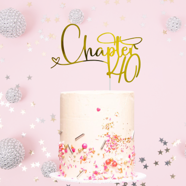 A cake with a gold "Chapter 40" topper on a pink background with decorative sparkles.