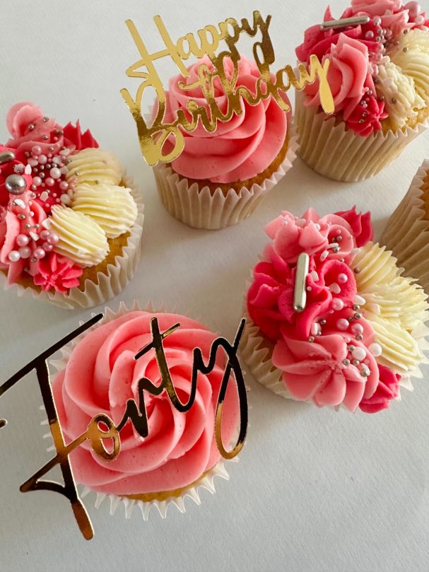 Colourful birthday cupcakes topped with pink frosting and decorative cake toppers.