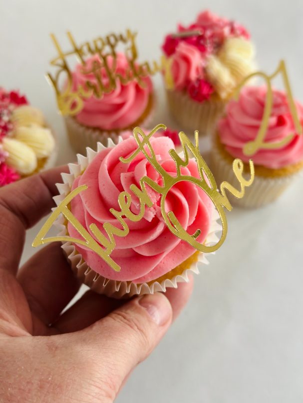 Hand holding a cupcake with pink frosting and a birthday topper reading "Twenty-Three".