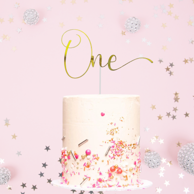 A decorated cake with a golden "One" topper, surrounded by festive confetti.