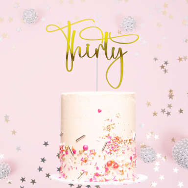 A decorated birthday cake with a "Thirty" topper and colourful sprinkles on a pink background.