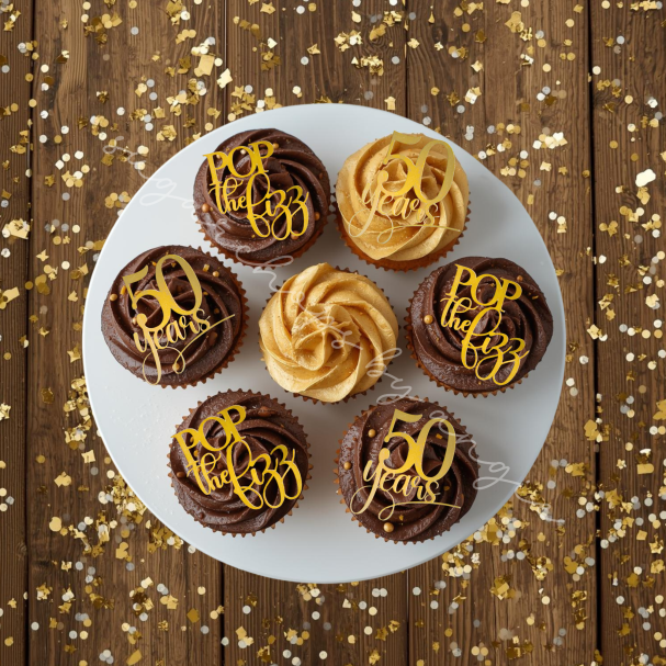 A selection of decorated cupcakes with "50" and gold frosting on a wooden surface.