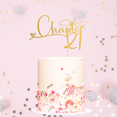 A pink birthday cake topped with a golden "Chapter 21" decoration and sparkles.