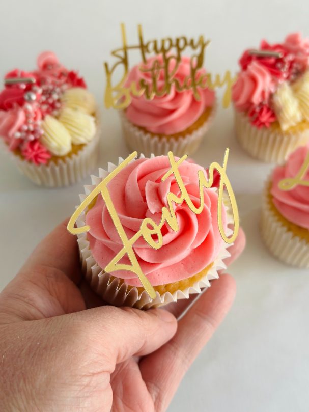 A hand holding a cupcake with pink frosting and a 'Happy Birthday' topper.