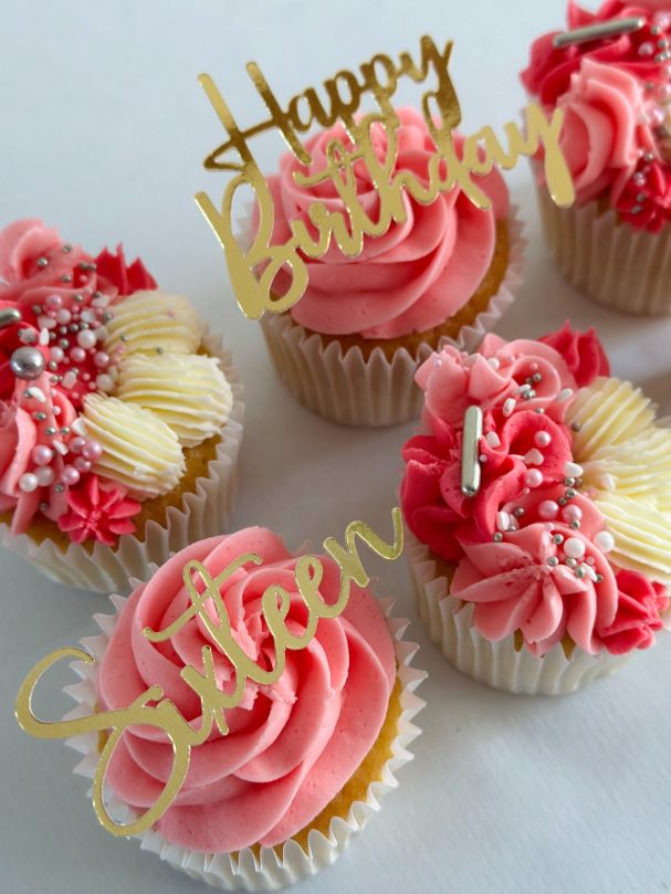 Pink frosted cupcakes decorated with "Happy Birthday" and "Sixteen" cake toppers.