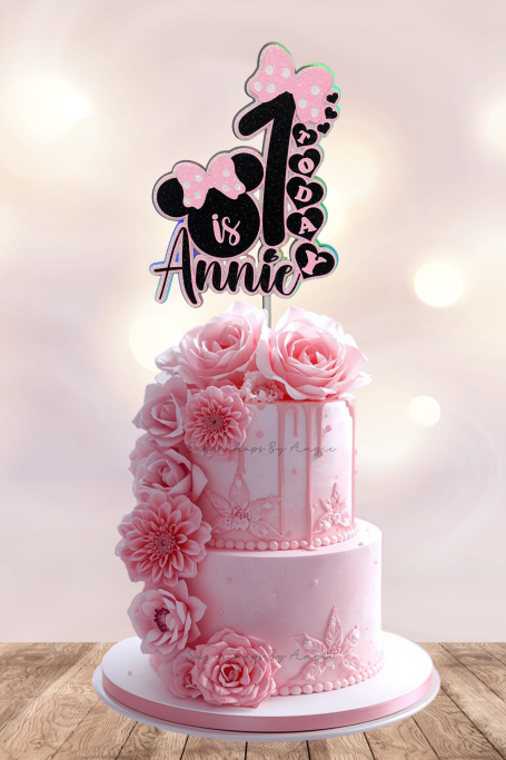 A two-tier pink birthday cake decorated with flowers and a "1" topper for Annie.