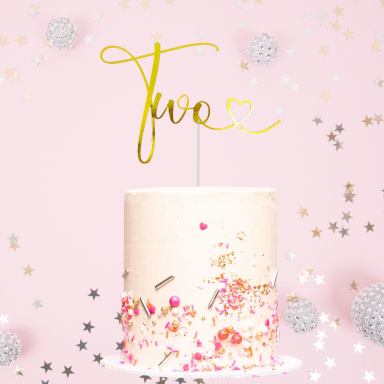 A two-tiered birthday cake with sprinkles and a gold "Two" cake topper.